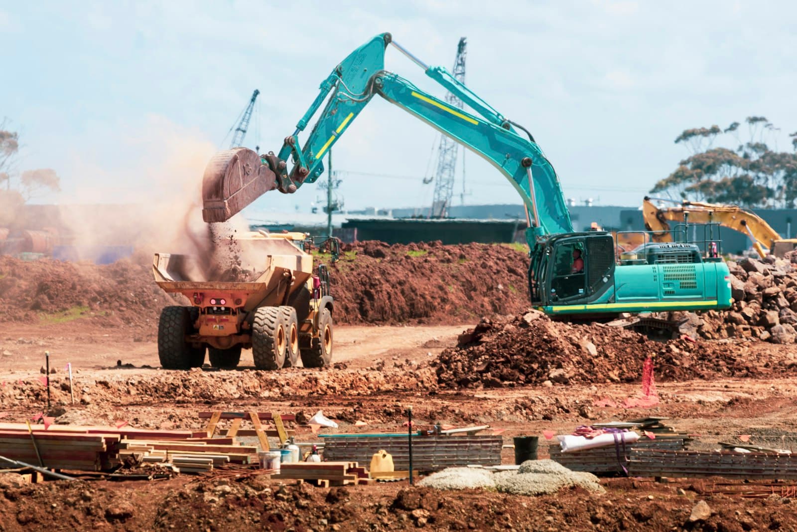 An excavator loading red dirt into a dump truck on an earthworks site